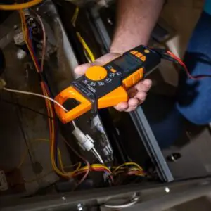 Inspecting an HVAC unit using voltage gauge with HVAC technicans hand